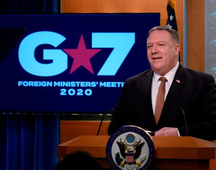 Mike Pompeo in a suit standing in front of a sign: Secretary of State Mike Pompeo speaks at the State Department on March 25 after a G-7 video conference.