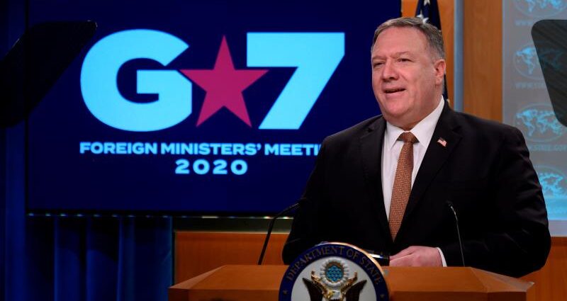 Mike Pompeo in a suit standing in front of a sign: Secretary of State Mike Pompeo speaks at the State Department on March 25 after a G-7 video conference.