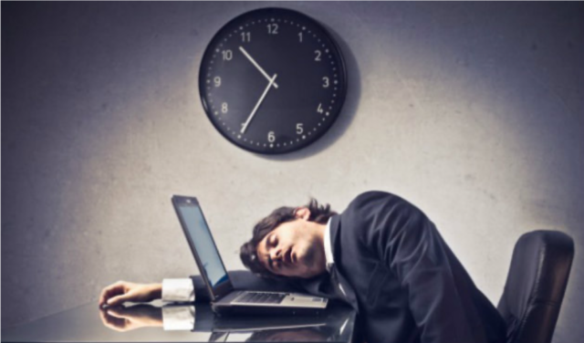 A person sitting at a desk with a computer and a clock Description automatically generated with low confidence