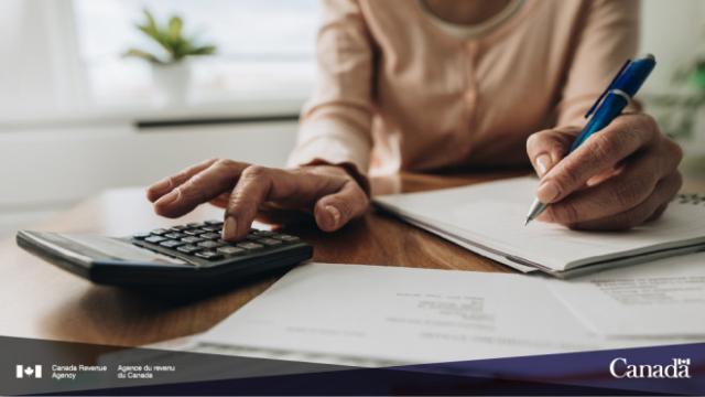 Someone at a desk writing on a notepad and using a calculator.