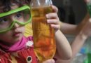 Child wearing safety goggles holding a bottle with liquid.