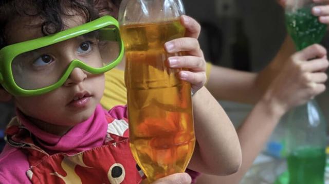 Child wearing safety goggles holding a bottle with liquid.