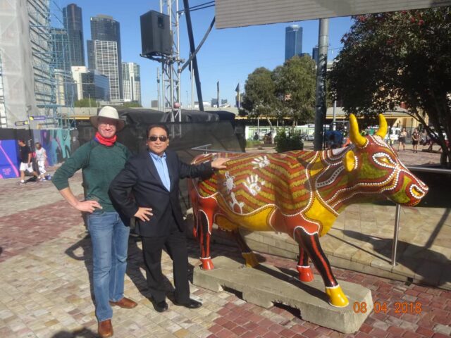 A couple of people posing with a statue of a cow Description automatically generated