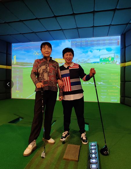 Two people standing in a room with a golf club Description automatically generated