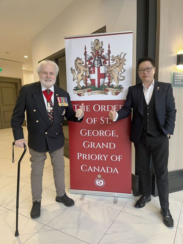 Two men standing in front of a sign Description automatically generated